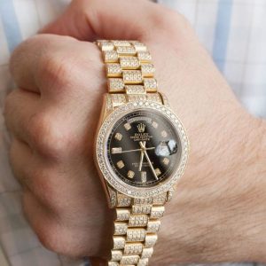 A gold Rolex wristwatch with a black dial and diamond accents is worn on a person's left wrist.