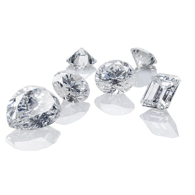 A group of variously cut loose diamonds, including round, pear, and emerald shapes, arranged on a white surface with reflections—similar to the gems assessed when considering how pawn shops evaluate diamond value in Atlanta.