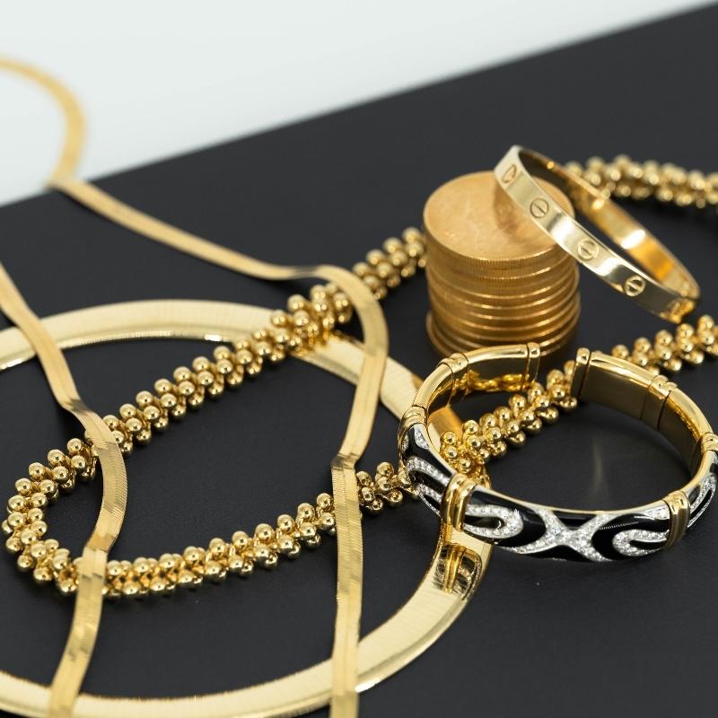 Assorted gold jewelry, including bracelets, necklaces, and a stack of coins, displayed on a black and white surface—perfect for those looking to pawn jewelry without receipts in Aventura.