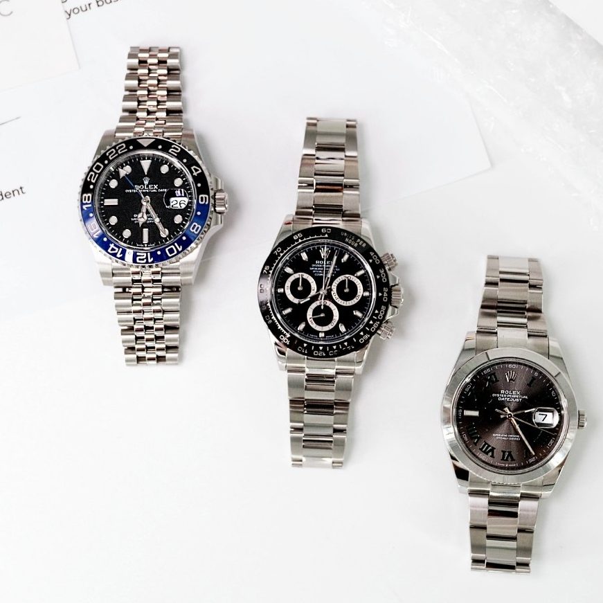 Three stainless steel wristwatches are displayed side by side on a white marble surface.