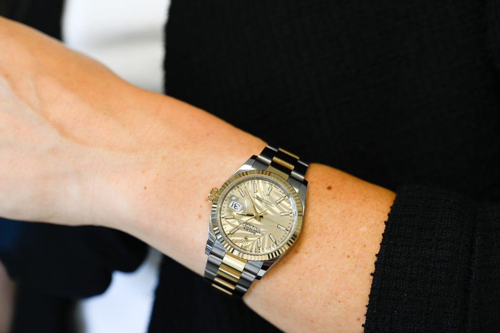 A close-up of a person's wrist wearing a two-tone metal wristwatch with a gold and silver band and a gold watch face.