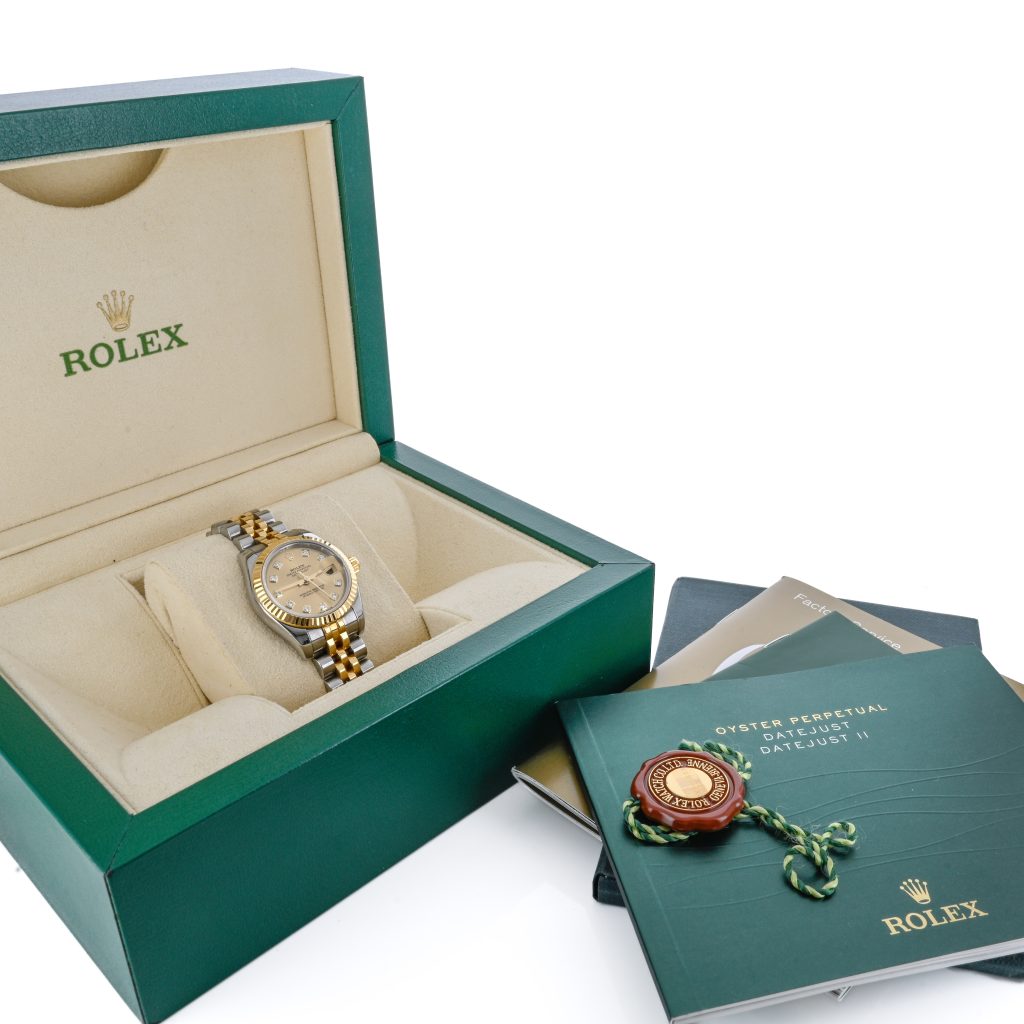 A Rolex watch in a green presentation box with official booklet, tag, and documents displayed beside it.