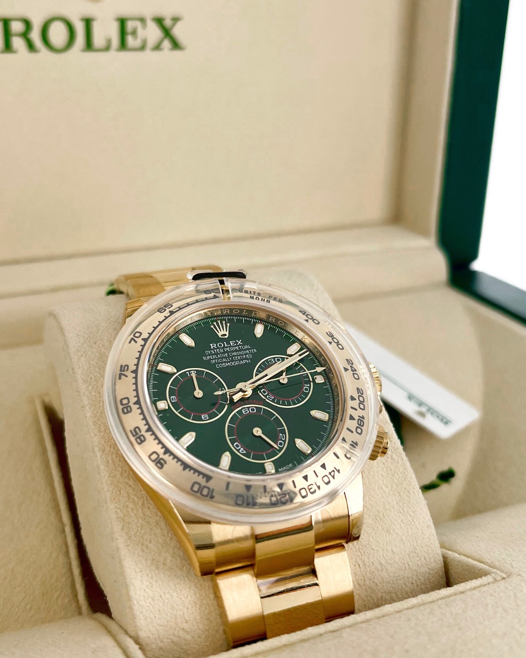 A gold Rolex Daytona watch with a green dial displayed in an open beige Rolex box.
