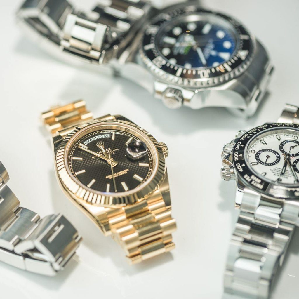 Three luxury wristwatches with metal bands—one gold and two silver—are displayed on a white surface, showcasing their detailed watch faces.