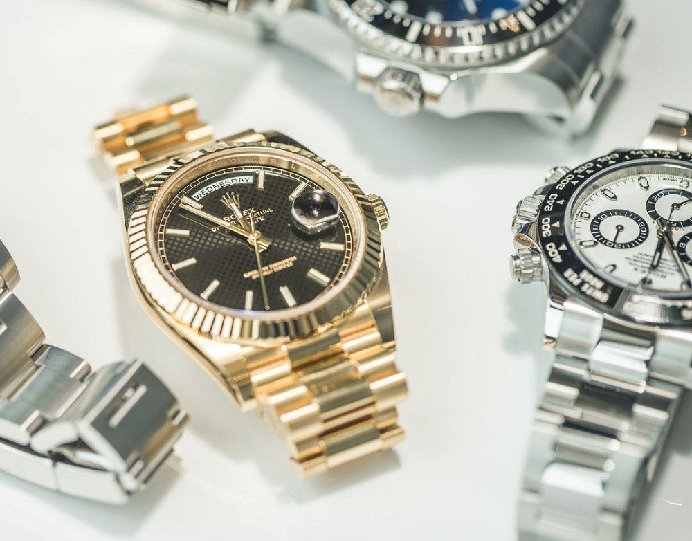 Several luxury wristwatches, including a gold watch with a black dial and metal bracelet, are displayed on a white surface—perfect for those looking to sell a Rolex with aftermarket parts in Atlanta.