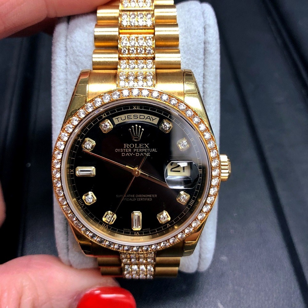A gold Rolex Oyster Perpetual Day-Date with a black dial, diamond hour markers, and a diamond-encrusted bezel and bracelet is held against a grey display cushion—perfect for those looking to pawn Rolex in Boca Raton.