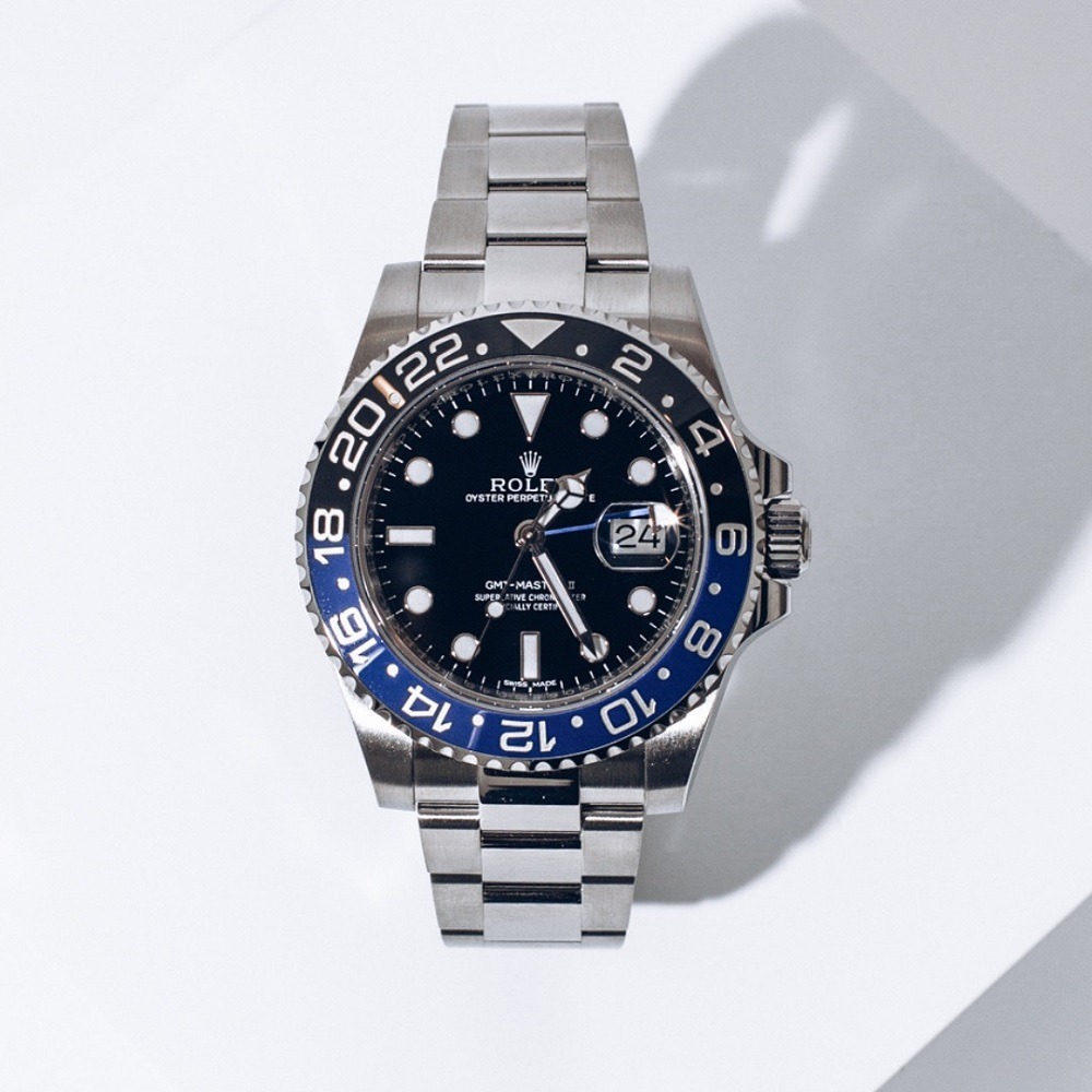 A silver Rolex GMT-Master II with a black and blue bezel, black dial, and date display sits on a white surface with shadows—perfect for those looking to sell a Rolex with aftermarket parts in Atlanta.