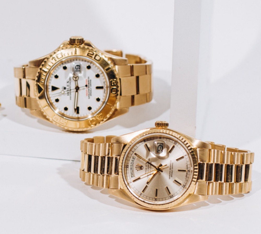 Two gold wristwatches are displayed on a white surface, one with a white dial and the other with a champagne dial, both featuring metal link bands—perfect selections for those seeking luxury at Rolex Pawn in Boca Raton.