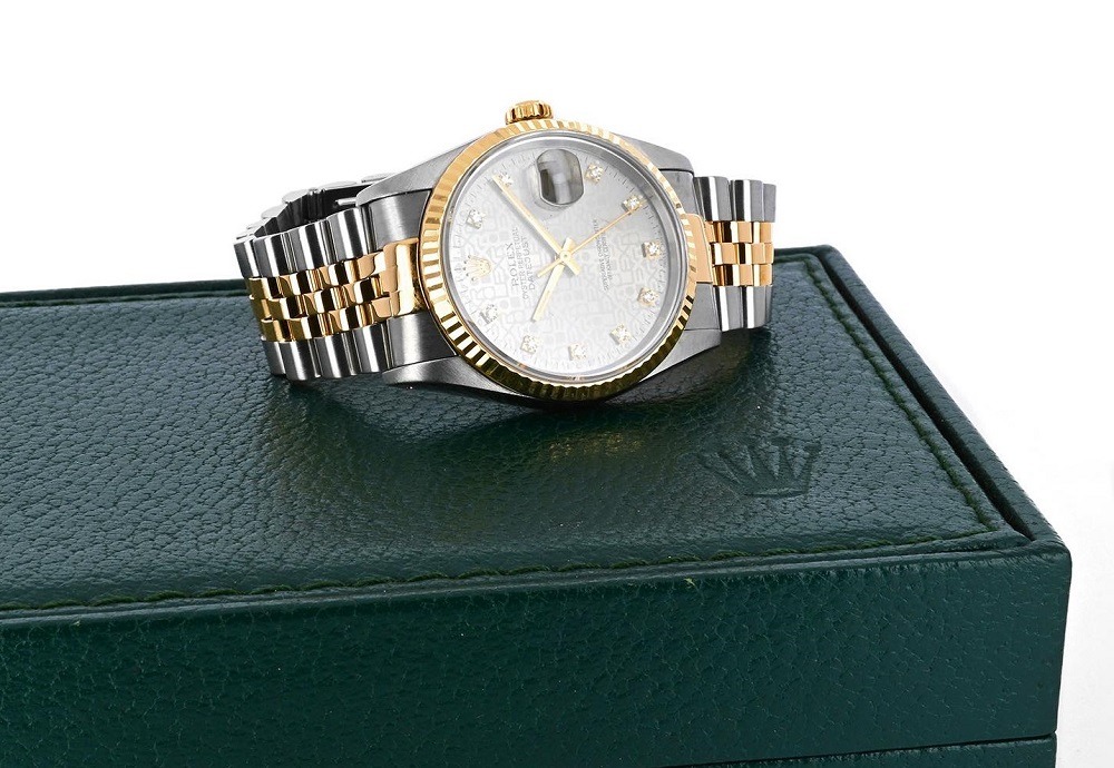 A two-tone wristwatch with a silver and gold bracelet is displayed on top of a green textured watch box featuring an embossed crown logo, available at Rolex Pawn in Boca Raton.